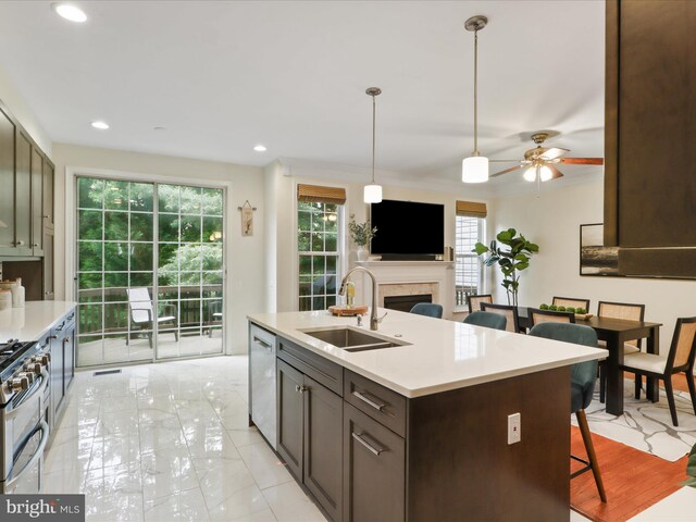 kitchen with a sink, appliances with stainless steel finishes, a fireplace, light countertops, and a ceiling fan