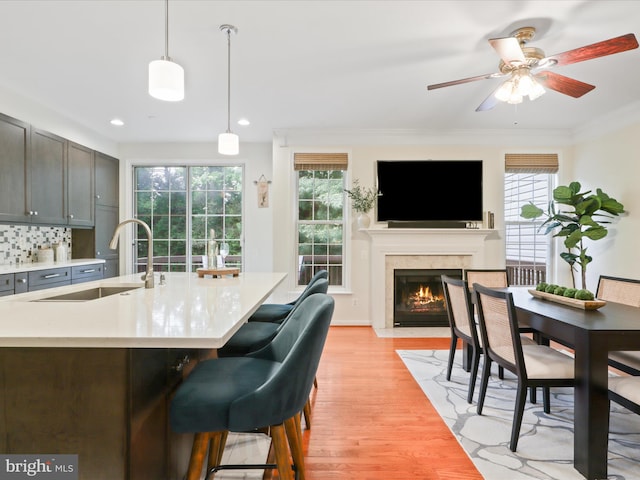 kitchen featuring a sink, light countertops, light wood-type flooring, a high end fireplace, and ceiling fan
