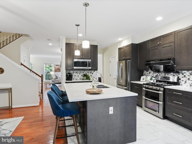 kitchen with stainless steel appliances, under cabinet range hood, a breakfast bar area, light countertops, and recessed lighting