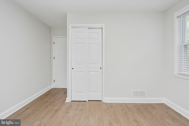 unfurnished bedroom featuring light wood finished floors, baseboards, and a closet