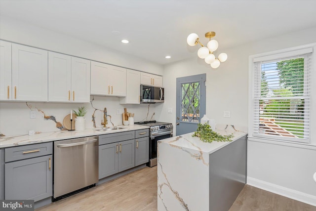 kitchen featuring stainless steel appliances, a sink, gray cabinets, light wood finished floors, and healthy amount of natural light