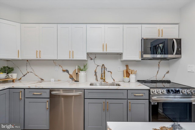 kitchen featuring appliances with stainless steel finishes, gray cabinets, a sink, light stone countertops, and white cabinetry