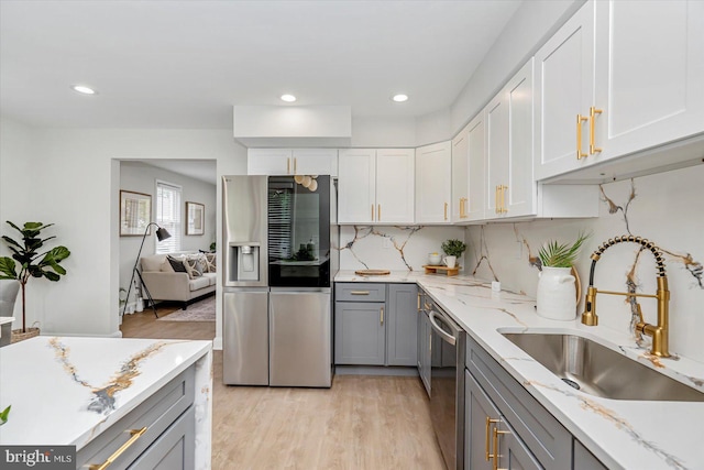 kitchen featuring stainless steel appliances, gray cabinets, a sink, light wood-style flooring, and light stone counters