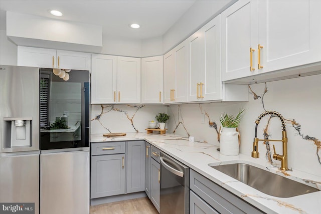 kitchen featuring appliances with stainless steel finishes, gray cabinetry, a sink, light stone counters, and decorative backsplash