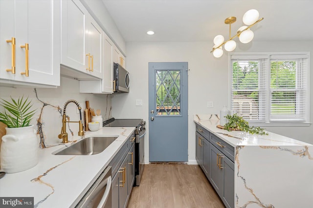 kitchen featuring stainless steel appliances, a sink, gray cabinetry, light wood-style flooring, and light stone counters
