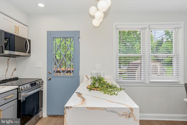 kitchen featuring appliances with stainless steel finishes, plenty of natural light, light wood finished floors, and light stone counters