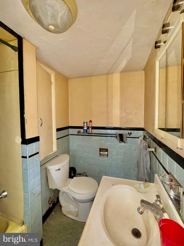 half bath featuring a sink, tile walls, wainscoting, and toilet