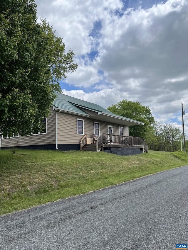 view of front facade with a wooden deck, a front lawn, and metal roof
