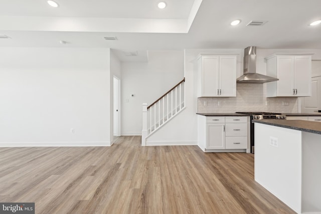 kitchen featuring wall chimney range hood, stainless steel gas range oven, dark countertops, light wood-type flooring, and tasteful backsplash