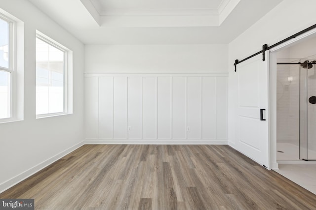 unfurnished bedroom featuring a barn door, wood finished floors, a raised ceiling, wainscoting, and a decorative wall
