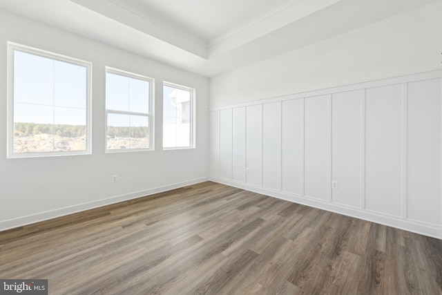 unfurnished room with a decorative wall, wood finished floors, wainscoting, ornamental molding, and a tray ceiling