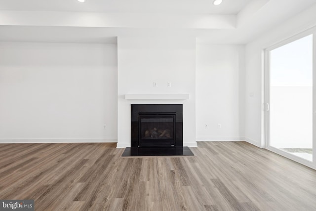 unfurnished living room with wood finished floors, recessed lighting, a fireplace with flush hearth, and baseboards