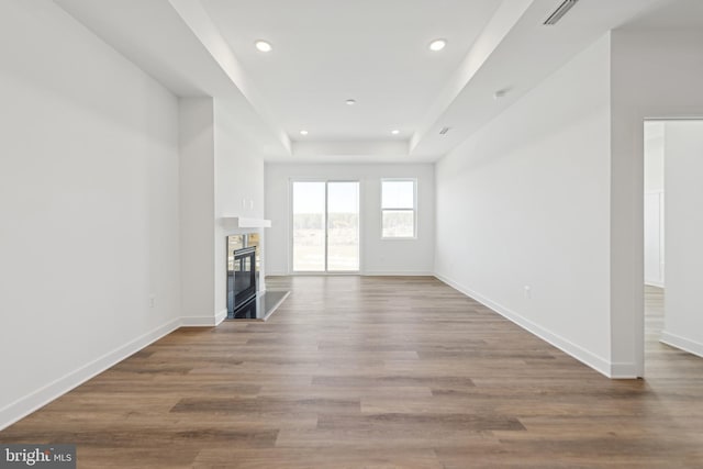 unfurnished living room with recessed lighting, baseboards, wood finished floors, a glass covered fireplace, and a tray ceiling