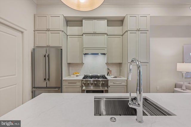 kitchen with high end appliances, a sink, ornamental molding, light stone countertops, and backsplash