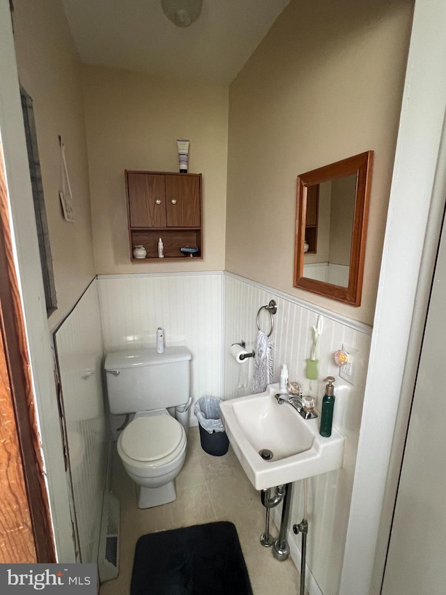 bathroom featuring wainscoting, toilet, a sink, and tile patterned flooring