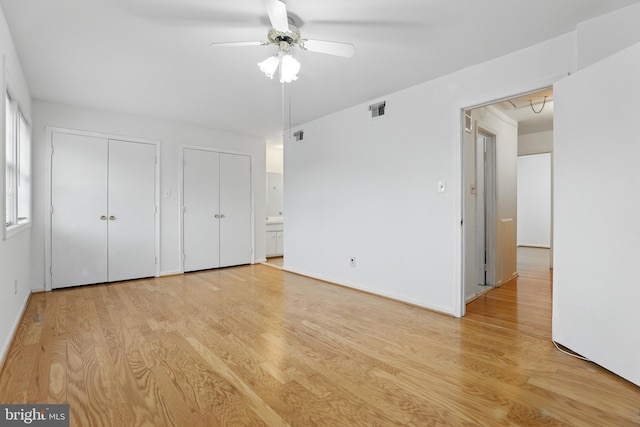 unfurnished bedroom featuring light wood-type flooring, two closets, ceiling fan, and baseboards