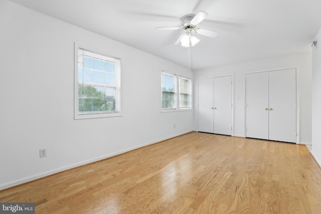 unfurnished bedroom with two closets, light wood-type flooring, baseboards, and ceiling fan