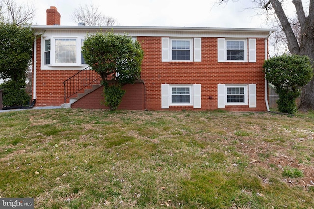 view of front facade featuring a chimney, brick siding, a front lawn, and stairs
