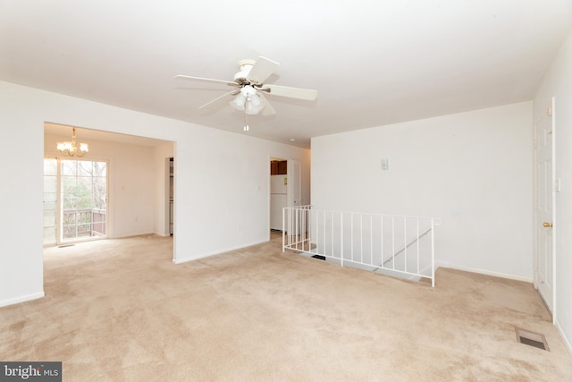 empty room featuring a chandelier, light colored carpet, baseboards, and a ceiling fan