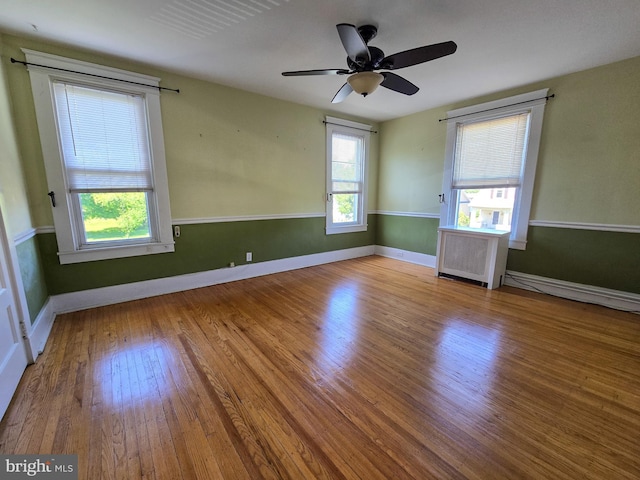 unfurnished room with plenty of natural light, wood finished floors, a ceiling fan, and baseboards