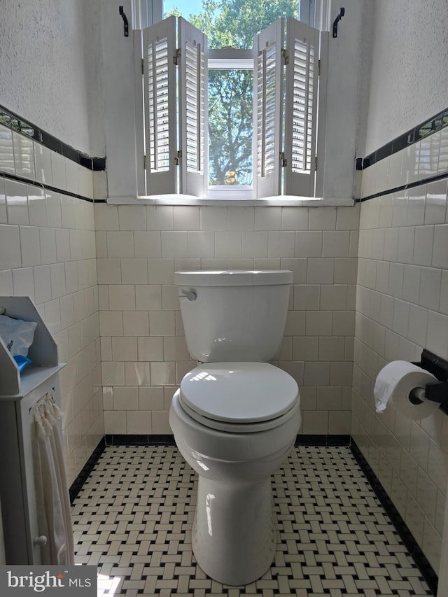half bath with tile walls, toilet, a wainscoted wall, and a textured wall