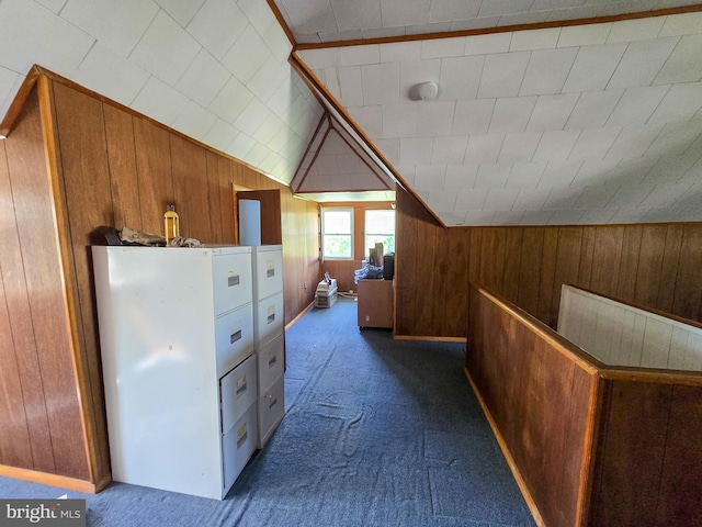 hallway with wooden walls, vaulted ceiling, and dark colored carpet
