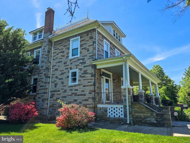 view of side of property with covered porch, stone siding, and a chimney