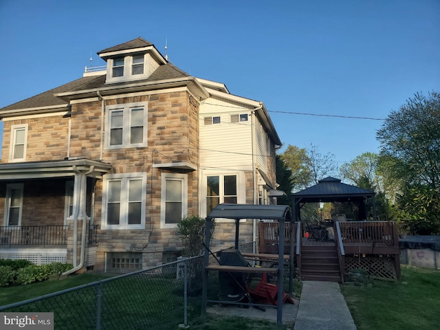 back of property with a gazebo, stone siding, and a deck