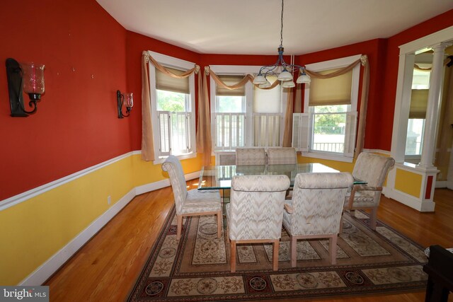 dining area with a chandelier, wood finished floors, baseboards, and ornate columns