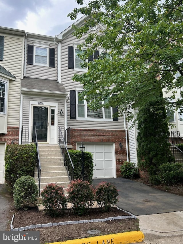 view of property with an attached garage, brick siding, and asphalt driveway