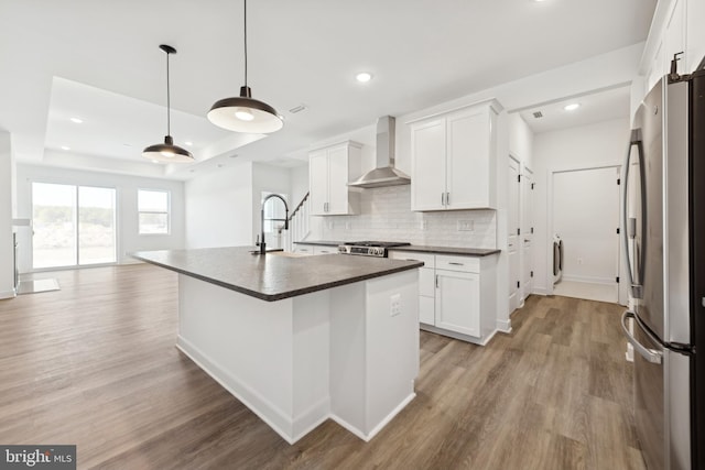 kitchen featuring freestanding refrigerator, wall chimney exhaust hood, dark countertops, a sink, and light wood finished floors