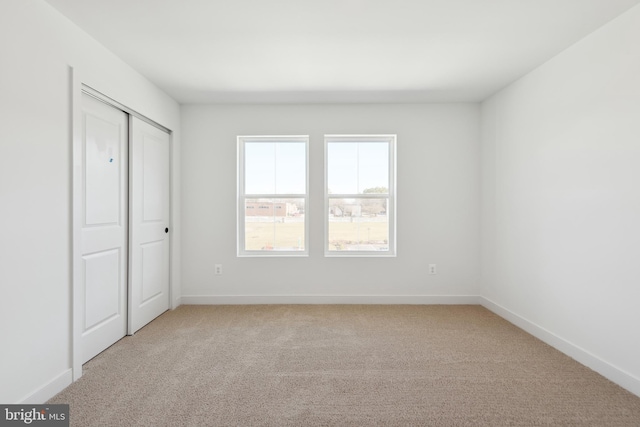 unfurnished bedroom with light colored carpet, baseboards, and a closet