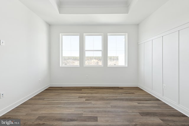 unfurnished room featuring a tray ceiling, dark wood finished floors, ornamental molding, and baseboards
