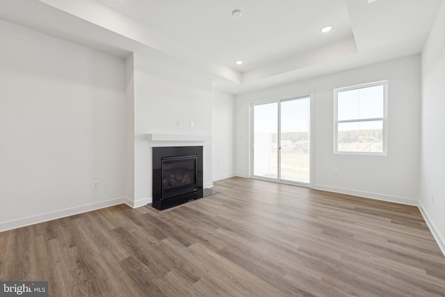 unfurnished living room featuring wood finished floors, baseboards, a fireplace with flush hearth, recessed lighting, and a raised ceiling