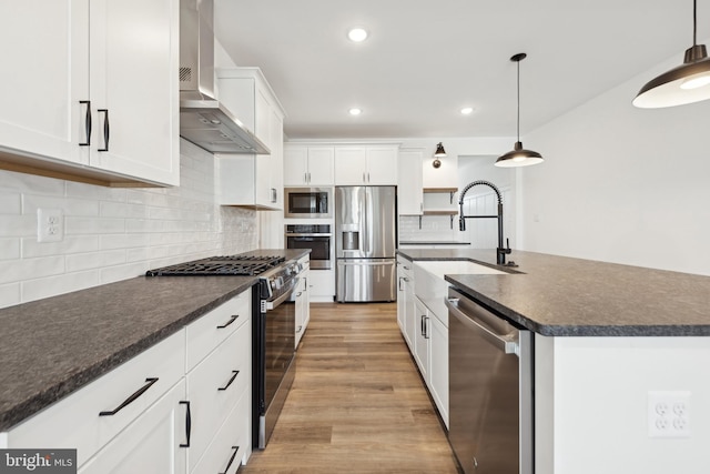 kitchen featuring stainless steel appliances, a sink, dark countertops, wall chimney exhaust hood, and light wood-style floors