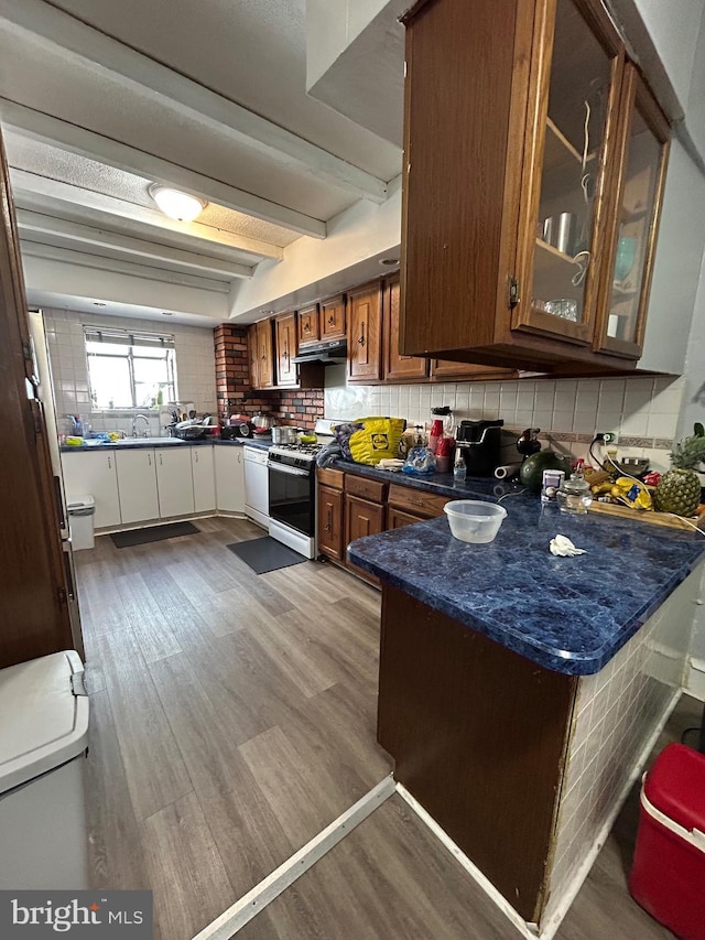 kitchen with gas range oven, wood finished floors, white dishwasher, tasteful backsplash, and beamed ceiling