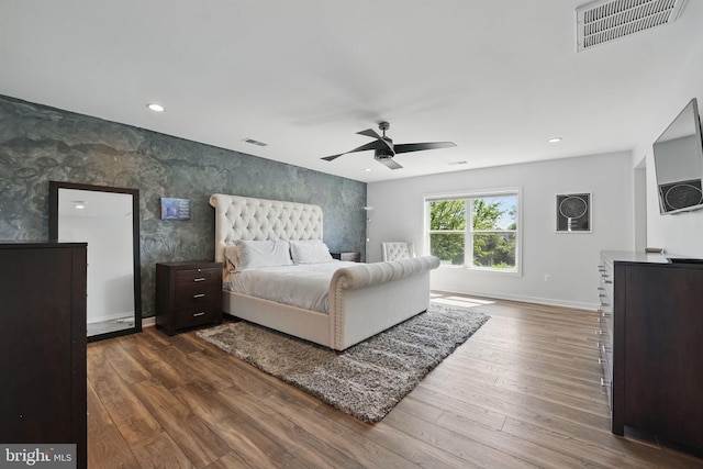 bedroom featuring wood finished floors, wallpapered walls, baseboards, a ceiling fan, and an accent wall