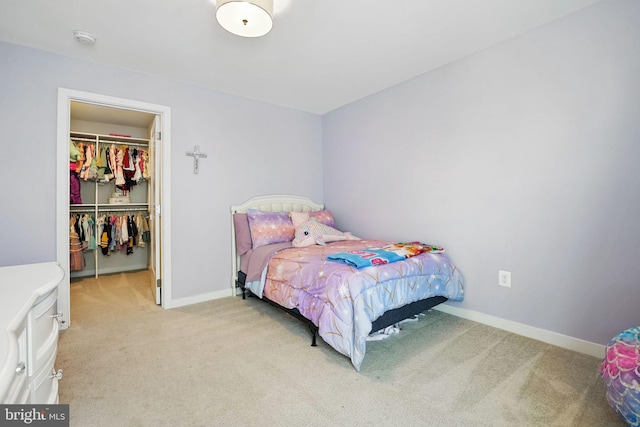 bedroom with a spacious closet, light colored carpet, a closet, and baseboards
