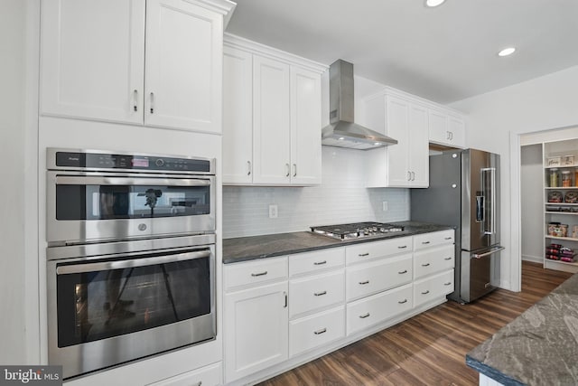 kitchen with appliances with stainless steel finishes, wall chimney exhaust hood, white cabinetry, backsplash, and dark wood-type flooring
