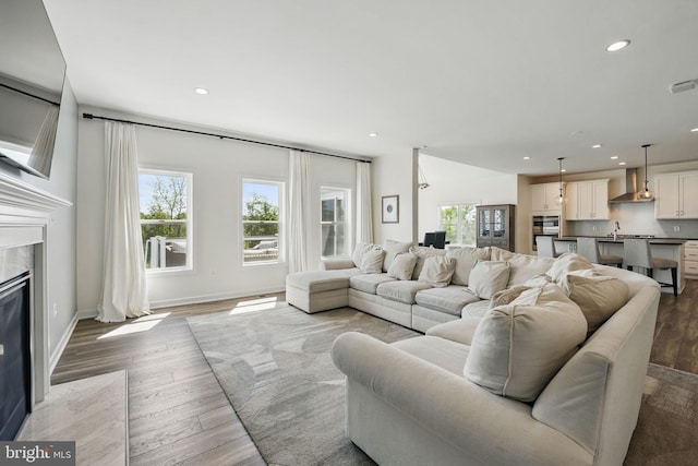 living room featuring healthy amount of natural light, recessed lighting, wood finished floors, a high end fireplace, and baseboards