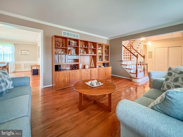 living room with stairs, light wood-type flooring, crown molding, baseboards, and a wainscoted wall