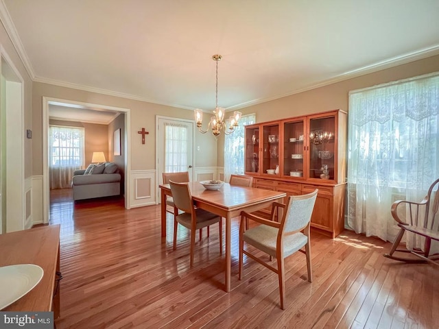 dining area with a chandelier, light wood-style flooring, wainscoting, crown molding, and a decorative wall