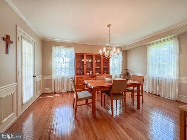 dining room featuring a chandelier, light wood-style floors, a wainscoted wall, ornamental molding, and a decorative wall