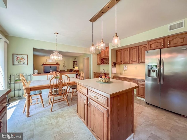 kitchen with stainless steel refrigerator with ice dispenser, light countertops, decorative light fixtures, a kitchen island, and brown cabinetry