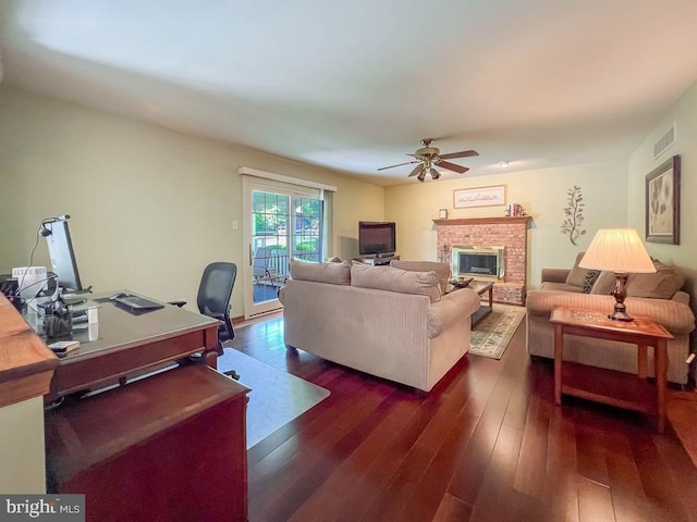 living area featuring dark wood finished floors, ceiling fan, an office area, and a brick fireplace