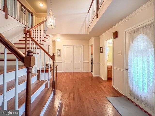 entryway featuring light wood-style floors, stairway, a chandelier, crown molding, and baseboards