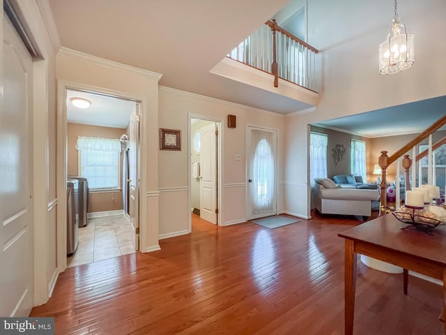 foyer entrance featuring ornamental molding, light wood-style flooring, baseboards, a chandelier, and stairway