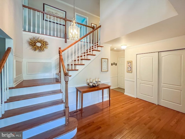 staircase with a decorative wall, wood finished floors, a chandelier, ornamental molding, and a towering ceiling