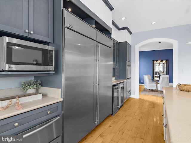 7839 Denton Ave, Baltimore, MD 21219 - kitchen featuring appliances with stainless steel finishes, a chandelier, light countertops, light wood-style floors, and arched walkways