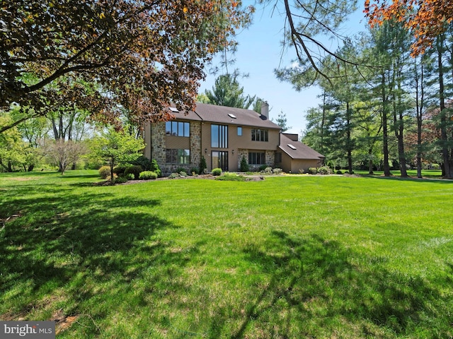 rear view of house with stone siding, a chimney, and a yard